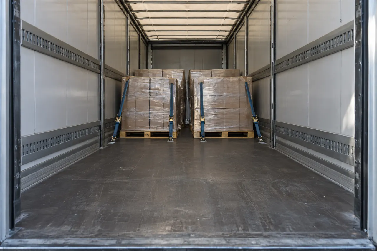 Palets bien trincados dentro de un tráiler cargado a medias, con la luz entrando por las puertas.